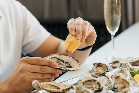 A man's hands squeezes fresh lemon juice onto an raw opened oyster, lifestyle food, ready to eat....
