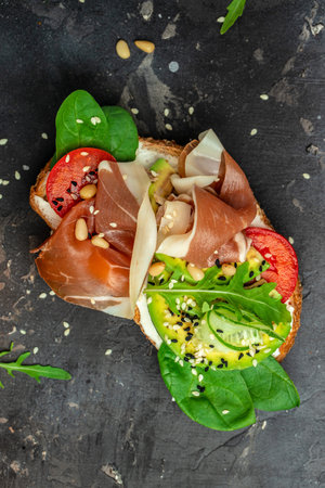 Open sandwich with prosciutto or jamon, avocado and fresh greens on a wooden board. Keto breakfast or snack, top view.の写真素材