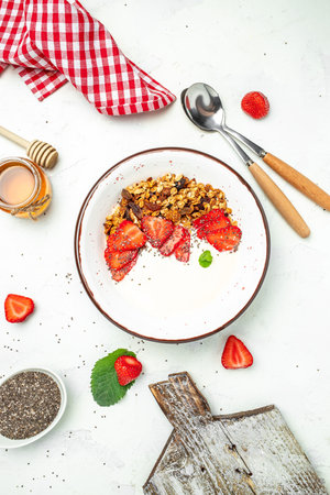 Bowl of homemade granola with fresh strawberry, chia seeds and honey on a light background. Delicious breakfast or snack. banner, menu, recipe place for text, top view.の写真素材