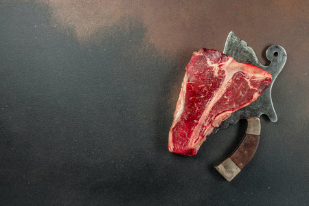 Meat Steaks T-bone between knife, on black stone background. Raw beef meat. place for text, top view.の写真素材