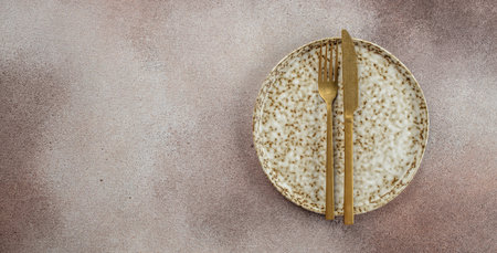 Empty plate, gold fork and knife on a light background. Long banner format. top view.の写真素材
