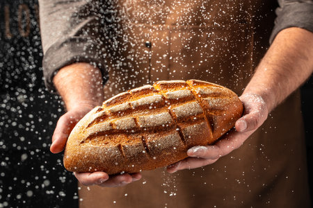male hands holding corn bread with powder in a freeze motion of a cloud of powder midair. Hands kneading raw dough. Culinary, cooking, bakery concept.の写真素材