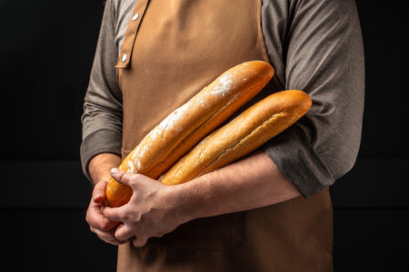 baguette in hand. bread in baker hands. bakery products on a dark background. The concept of baking bakery products.の写真素材
