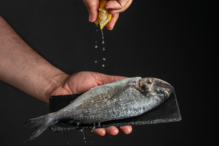 man hands holds dorado fish with Freeze motion splash drops of lemon juice on black background. place for text.の写真素材