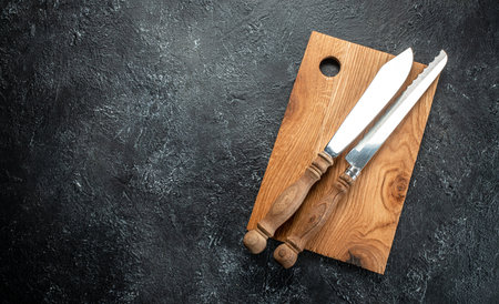 cooking background with wooden cutting board and sharp knives on a dark background. place for text,...