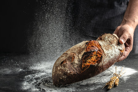 Male hands with fresh baked loaf rye wheat bread on a dark background, place for text, top view,