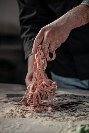 men hands holding sliced pastry for pasta on a dark background. home cooking concept.の写真素材