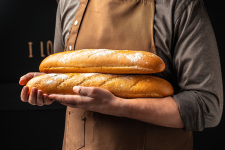 baguette in hand. bread in baker hands. bakery products on a dark background.の写真素材