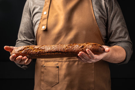 baguette in hand. bread in baker hands. bakery products on a dark background. The concept of baking bakery products.の写真素材