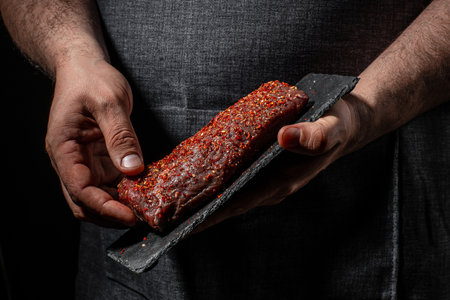 cooking meat steak and adding seasoning, beef steaks with grilled spices on dark background. Restaurant menu, dieting, cookbook recipe.の写真素材