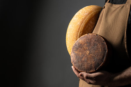hands holding wheel hard cheese on a dark background, cheese producer, place for text,の写真素材