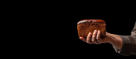 kraft square rye loaf of bread in hand on black background, Long banner format. copy space for text,