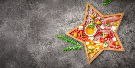 Antipasto platter with ham, prosciutto, salami, cheese, crackers and olives on the board in the form of a Christmas star. Christmas table.の写真素材