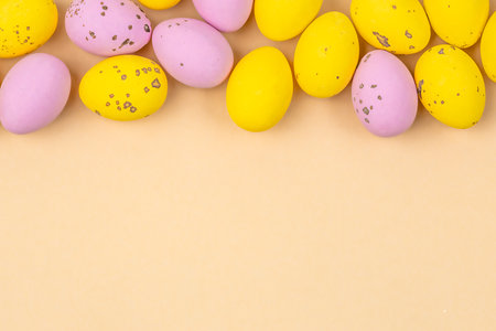 Small speckled multicolored chocolate eggs set close-up on a yellow background. Top view.