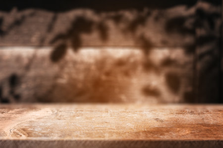 A sunlit wooden table with soft leaf shadows on the wall creates a warm and inviting rustic backdrop for cozy meals or autumn moments.の写真素材