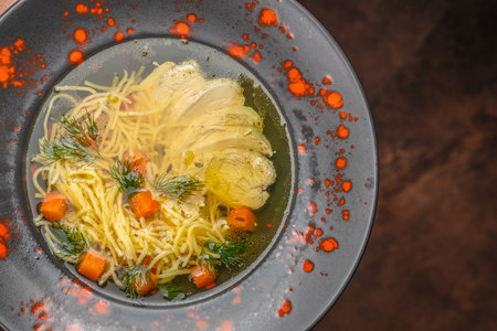 Clear chicken noodle soup with tender fillet slices, diced carrots, and fresh dill served in a rich golden broth for comforting warmth.の写真素材