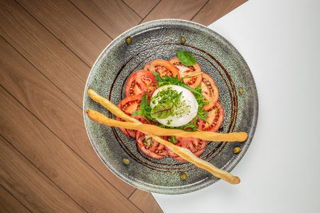 Fresh caprese salad with creamy burrata cheese, ripe tomato slices, green arugula, and crispy...