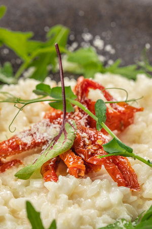 A close-up of creamy risotto topped with sun-dried tomatoes, parmesan cheese, and fresh green herbs, showing vibrant colors and rich textures.の写真素材