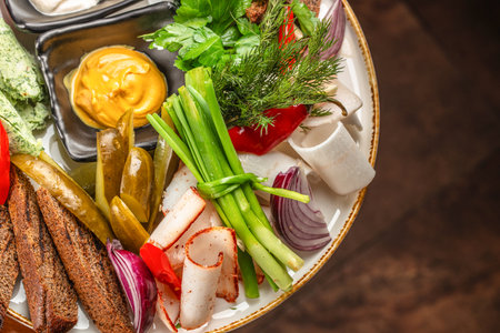 Rustic appetizer platter with assorted pickles, rye bread, mustard, fresh herbs, onion slices, lard, and seasoned cured meat rolls.の写真素材