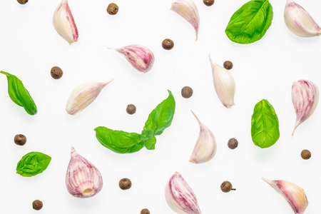 Flat lay of garlic cloves, basil leaves, and peppercorns on white background.の写真素材