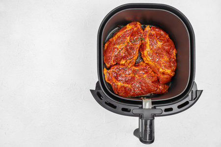 Top view of marinated pork steaks in an air fryer basket on a light surface with copy space.の写真素材