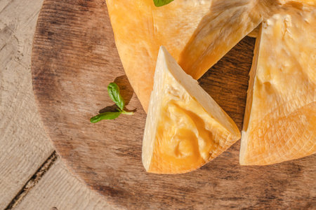 A close-up view of a smoked cheese wedge cut from a round block, resting on a rustic wooden board...