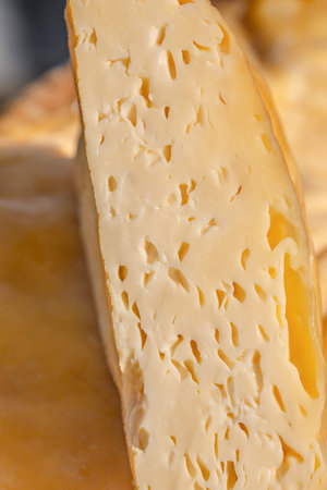 A close-up view of a wedge of semi-hard smoked cheese shows its smooth texture and tiny holes, highlighting its rich, creamy interior and golden rind.の写真素材