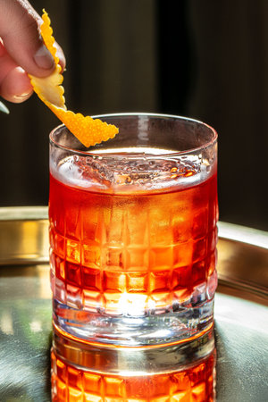 A classic cocktail served in a textured glass with a vibrant orange twist garnish, capturing a...