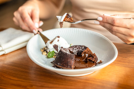A woman enjoys a rich chocolate lava cake with vanilla ice cream and nuts in a cozy dessert setting....
