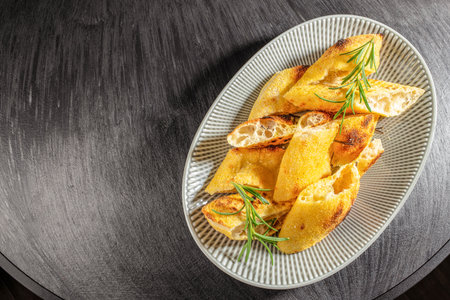 Freshly baked rustic bread slices garnished with rosemary are served on a ceramic plate over a dark wooden table. top view. copy space.の写真素材