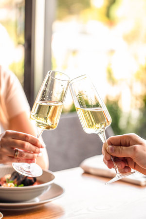 Two people toast with glasses of champagne in a bright and elegant dining setting.