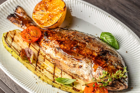 grilled whole dorado fish with vegetables and lemon on a white plate. top view.