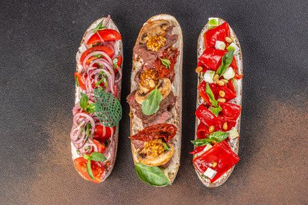 Assorted gourmet bruschetta with vegetables, mushrooms, and herbs on dark background.の写真素材