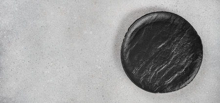 Black round plate on light concrete background, top view, copy space.の写真素材