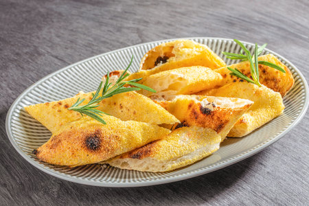 Crispy focaccia bread pieces sprinkled with cornmeal and garnished with fresh rosemary on a ceramic...