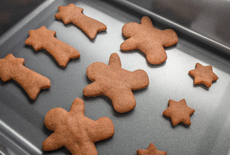 Freshly baked gingerbread cookies in various shapes on a baking tray, close up.