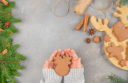 Cozy holiday concept with hands holding a reindeer-shaped gingerbread cookie surrounded by Christmas...