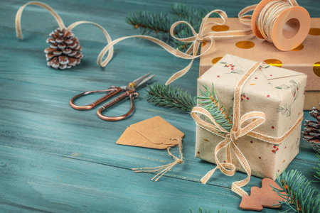 Festive holiday composition with beautifully wrapped Christmas gifts, rustic twine, pine branches, and craft tools on a turquoise wooden background. copy space.の写真素材
