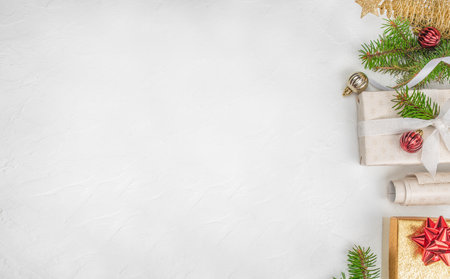 Minimalistic Christmas flat lay with gift boxes, fir branches, and red and gold ornaments on white background with wide copy space on the left elegant holiday composition for greetings or advertising.の写真素材