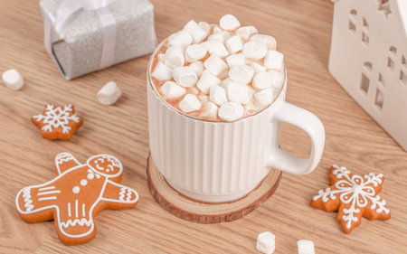 Cup of hot chocolate with marshmallows and gingerbread cookies on wooden table, cozy winter holiday scene with festive gift box and warm Christmas atmosphere, close-upの写真素材