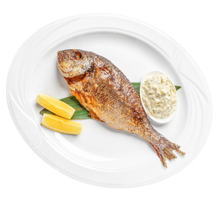 Grilled whole dorado fish with lemon wedges and creamy sauce on white plate, top view elegant...