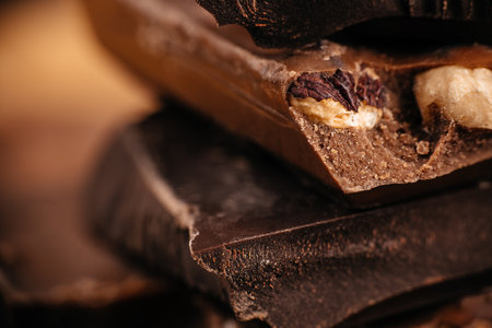 Close-up macro of stacked chocolate pieces with whole nuts showing rich texture and soft warm tones...