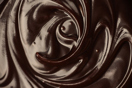 Close-up swirl of melted glossy dark chocolate creating smooth rich texture perfect for dessert design, confectionery branding and sweet food advertising backgroundsの写真素材