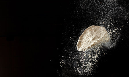 Dynamic flour burst with flying dough on dark background for bakery and cooking advertising.の写真素材