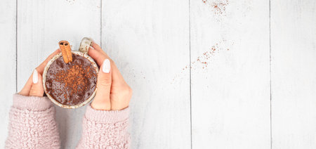 Female hands holding cup of hot chocolate with cinnamon, top view, white background with copy space.の写真素材