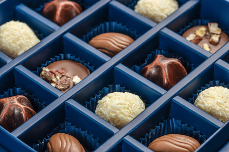 Close-up view of luxury assorted chocolate pralines in elegant blue gift box, showcasing textures...
