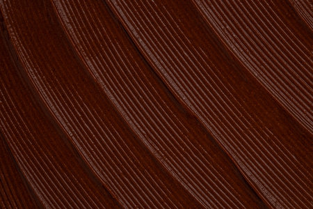 Macro texture of chocolate spread with diagonal striped pattern and glossy surface, rich dark brown...