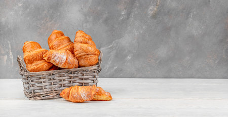 Golden flaky croissants in wicker basket on rustic gray background with copy space, classic French bakery breakfast concept for menu, packaging or food advertisingの写真素材