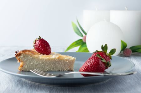 Cheesecake with strawberries on a gray plate on the table with candles.の写真素材