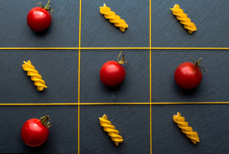 Tic-tac-toe from pasta and tomatoes on a dark background.の写真素材